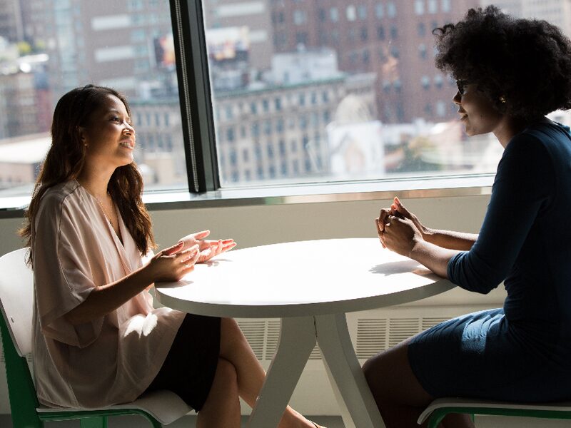 Two colleagues in conversation across a table beside a window overlooking the city